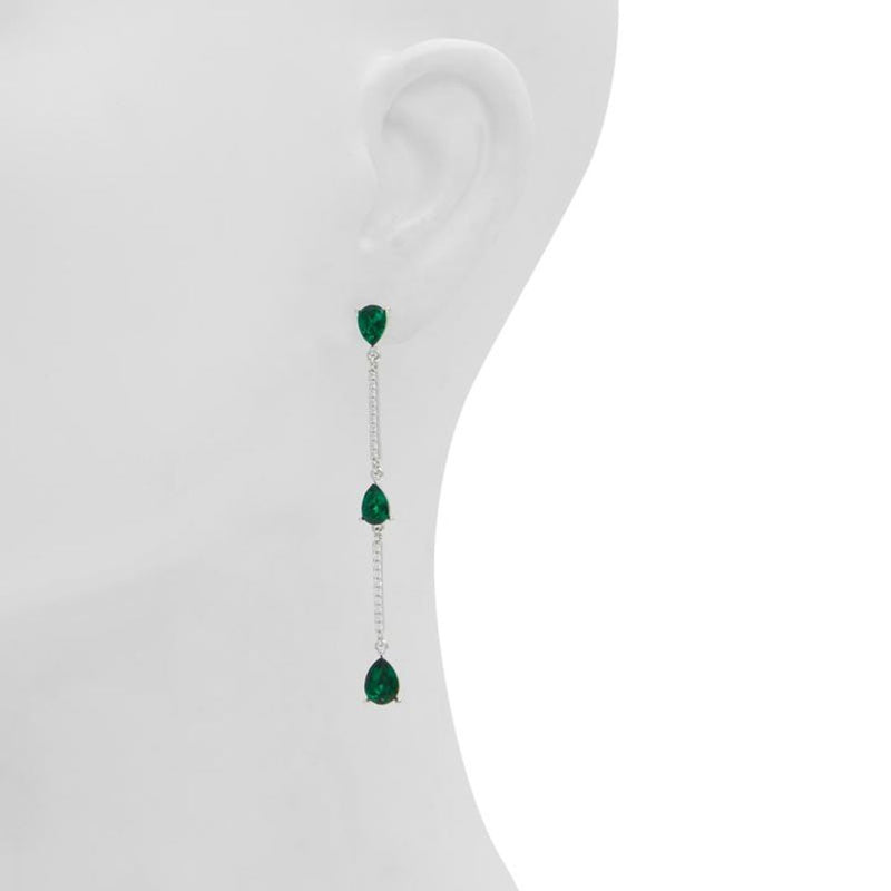 Long silver dangle earrings featuring three teardrop-shaped green stones worn on an earlobe