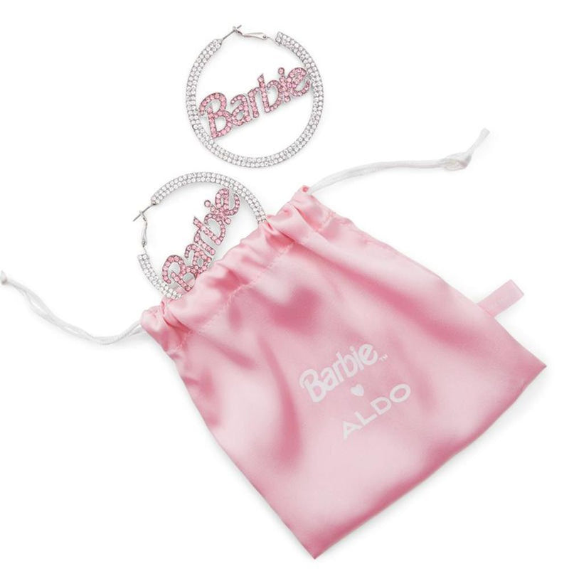 Silver crystal hoop earrings with pink Barbie lettering next to a pink satin drawstring bag