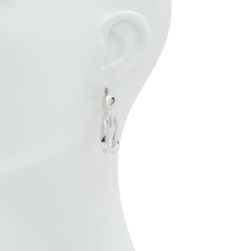 Glossy silver twisted hoop earrings worn on a white mannequin ear