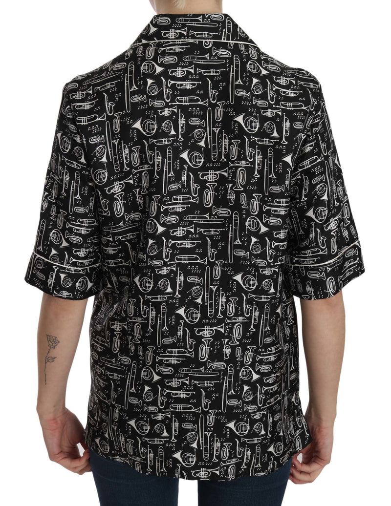 Black silk short-sleeve top with white musical instrument print and a collared neckline worn by a person