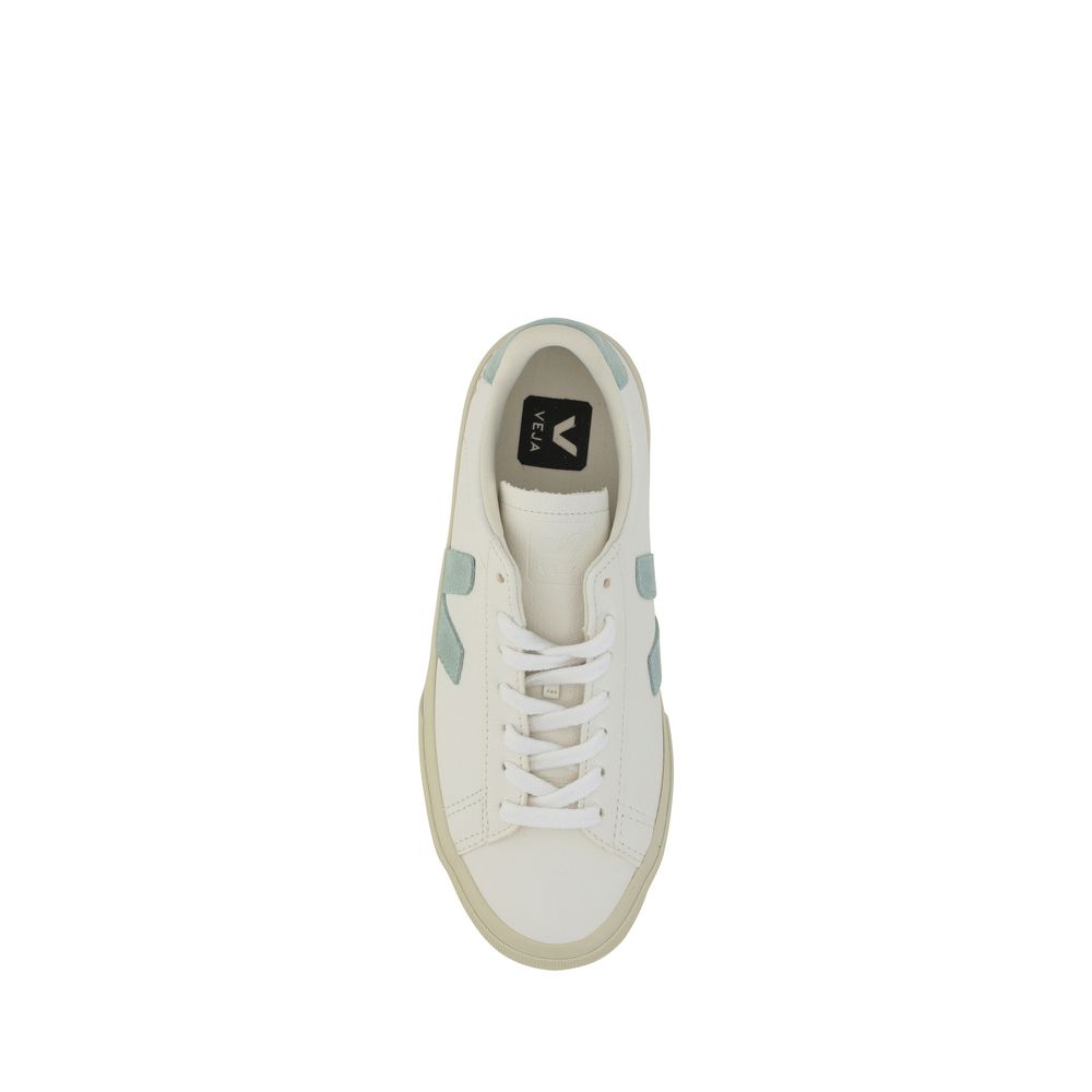 White calf leather Veja sneaker with light blue suede V logo and heel tab, white laces, and a cream rubber sole.
