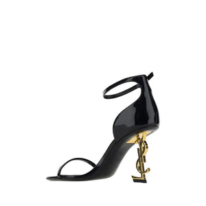 Saint Laurent black calf leather heeled sandals with an iconic gold-tone YSL logo heel and ankle strap.