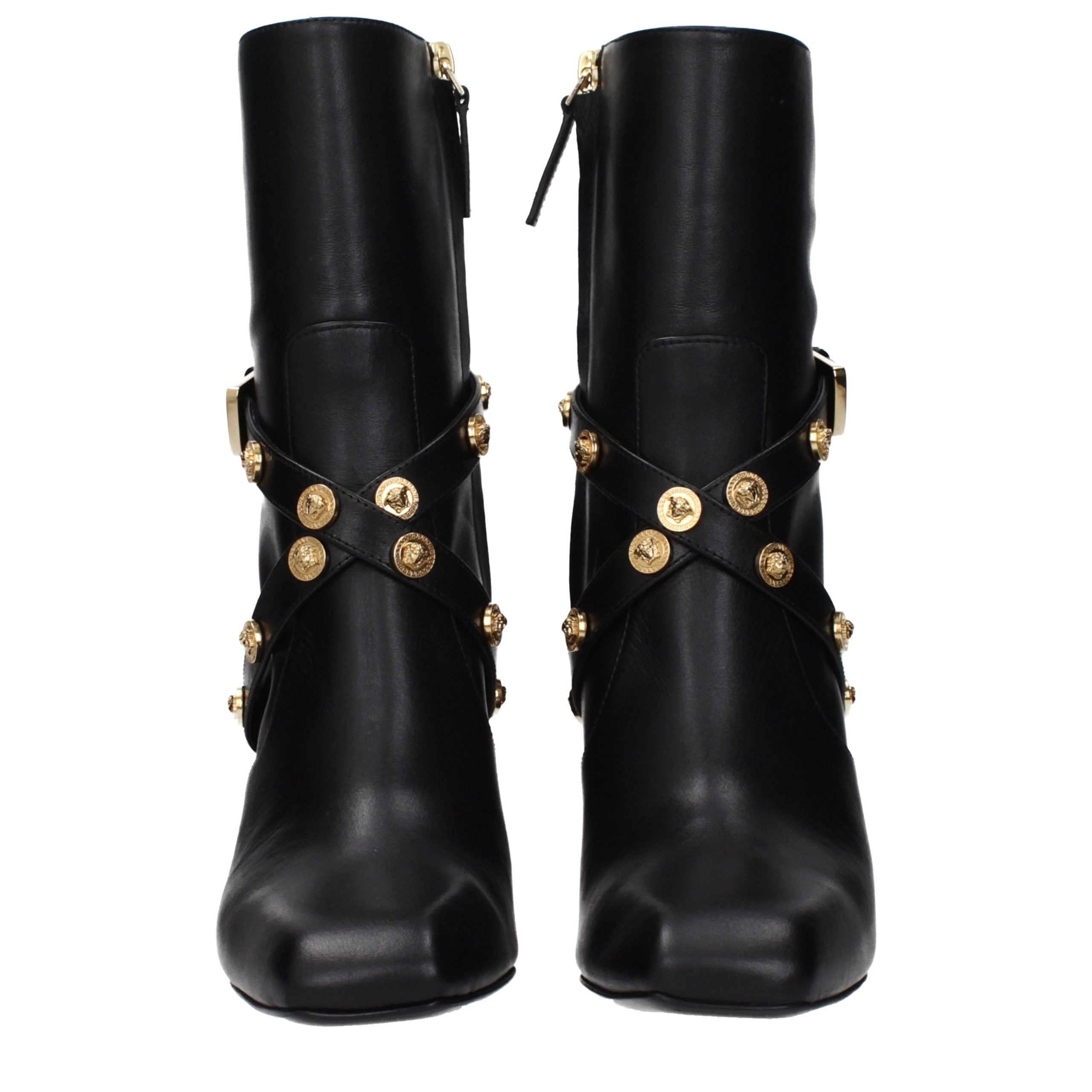 Female model wearing Versace black leather ankle boots with a sleek black leather upper, structured silhouette, and premium luxury finish, captured mid-step in a casual lifestyle pose showcasing the boot's bold profile and iconic Italian craftsmanship.