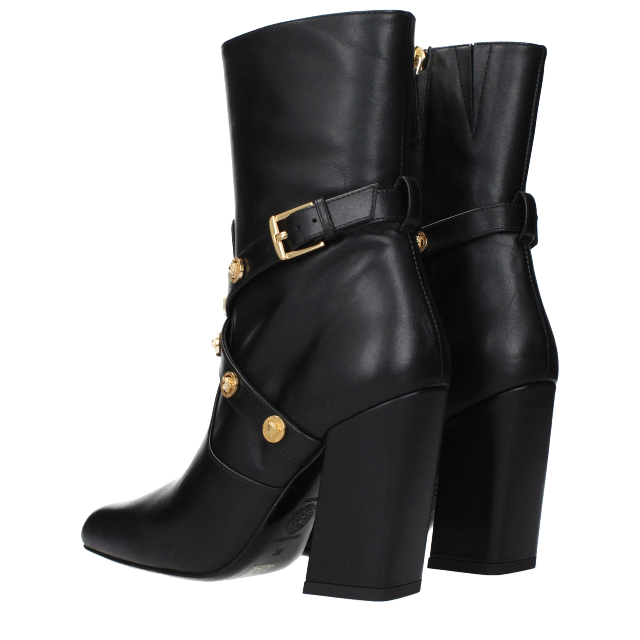 Female model wearing Versace black leather ankle boots with a sleek black leather upper, structured silhouette, and premium luxury finish, captured mid-step in a casual lifestyle pose showcasing the boot's bold profile and iconic Italian craftsmanship.