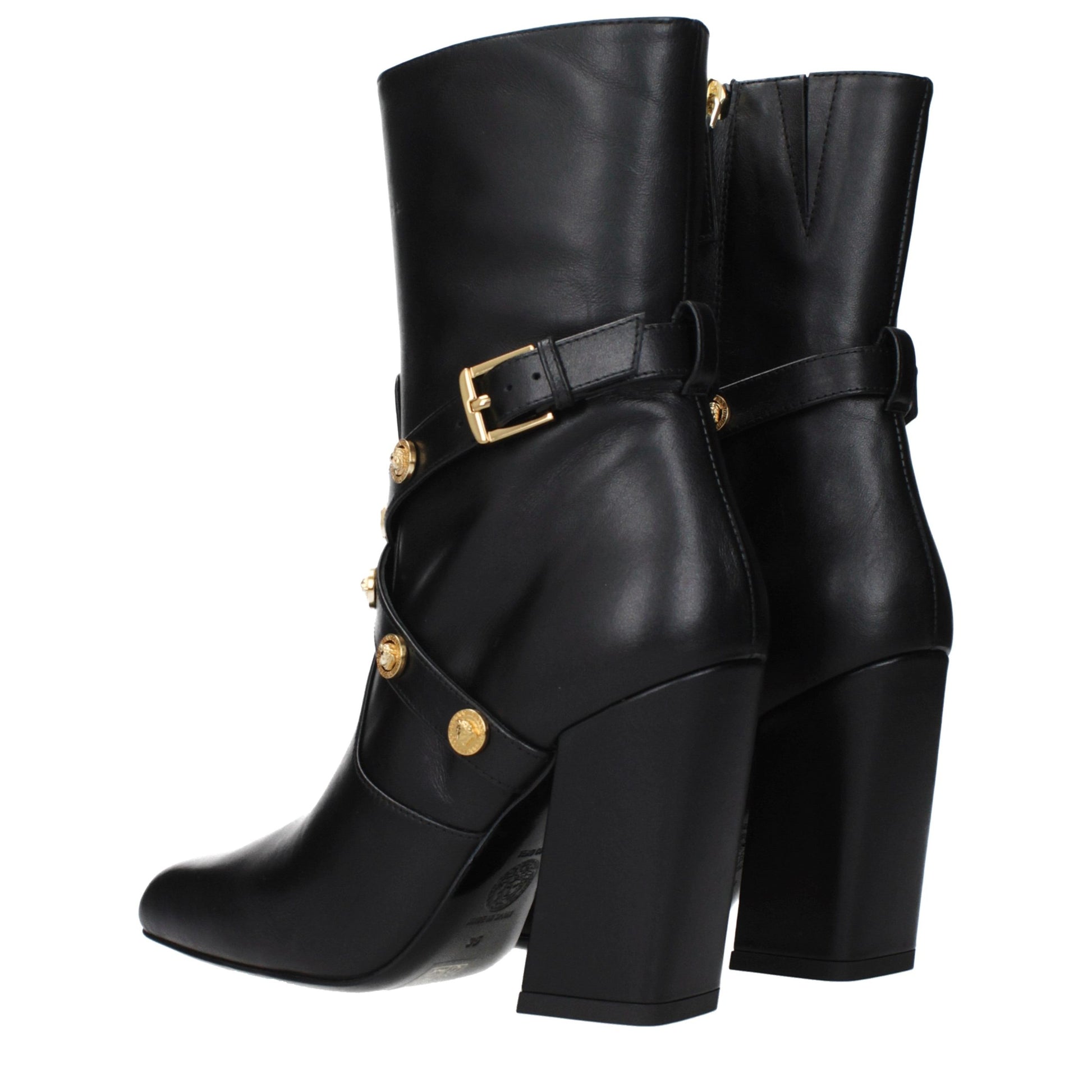 Female model wearing Versace black leather ankle boots with a sleek black leather upper, structured silhouette, and premium luxury finish, captured mid-step in a casual lifestyle pose showcasing the boot's bold profile and iconic Italian craftsmanship.