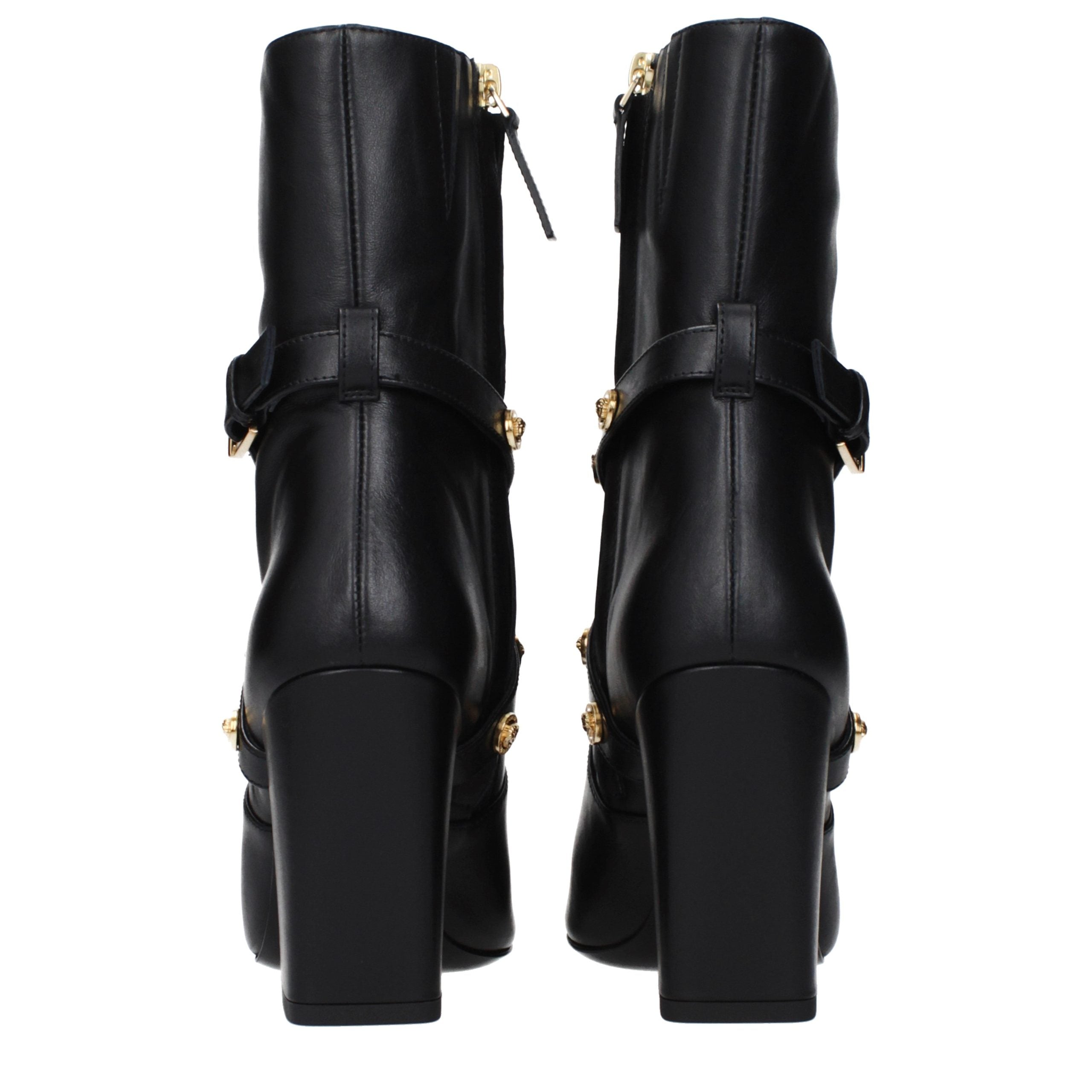 Female model wearing Versace black leather ankle boots with a sleek black leather upper, structured silhouette, and premium luxury finish, captured mid-step in a casual lifestyle pose showcasing the boot's bold profile and iconic Italian craftsmanship.