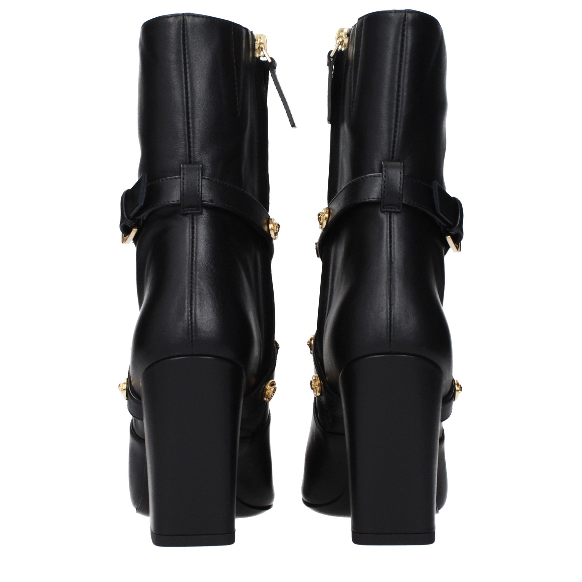 Female model wearing Versace black leather ankle boots with a sleek black leather upper, structured silhouette, and premium luxury finish, captured mid-step in a casual lifestyle pose showcasing the boot's bold profile and iconic Italian craftsmanship.