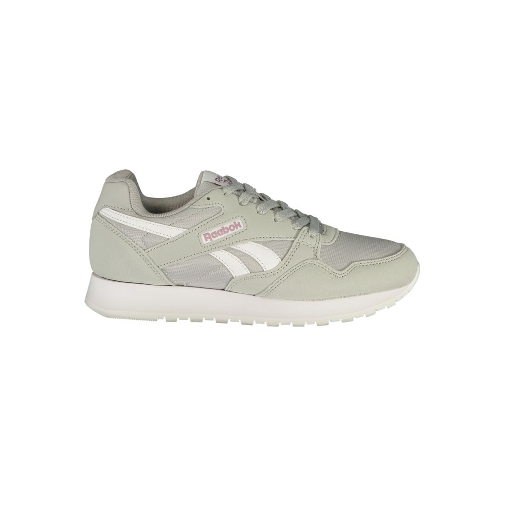 Female model wearing Reebok sage gray women's sneakers with a soft sage mixed mesh and suede upper, iconic white Reebok vector logo, subtle pink accent branding, and chunky white platform sole, captured mid-step in a casual lifestyle pose showcasing the sneaker's retro athletic silhouette and everyday versatility.