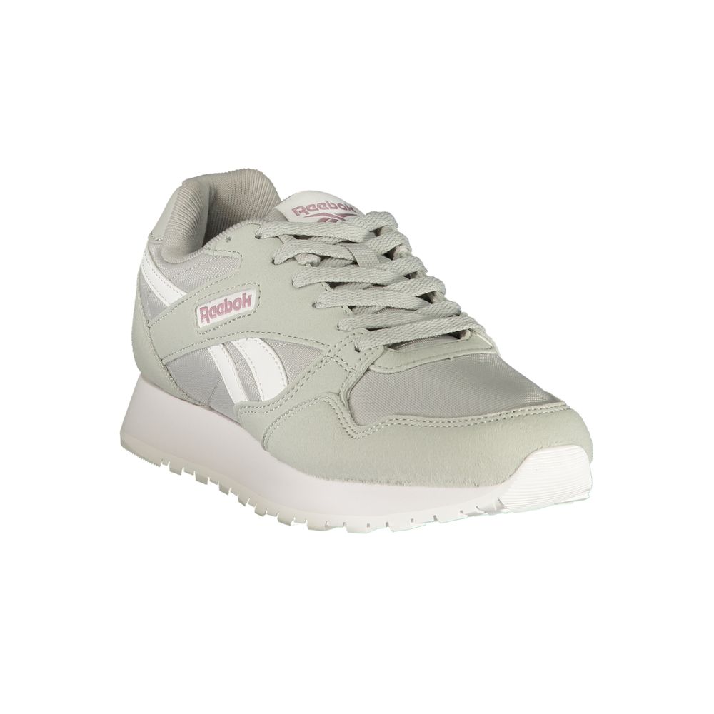 Female model wearing Reebok sage gray women's sneakers with a soft sage mixed mesh and suede upper, iconic white Reebok vector logo, subtle pink accent branding, and chunky white platform sole, captured mid-step in a casual lifestyle pose showcasing the sneaker's retro athletic silhouette and everyday versatility.