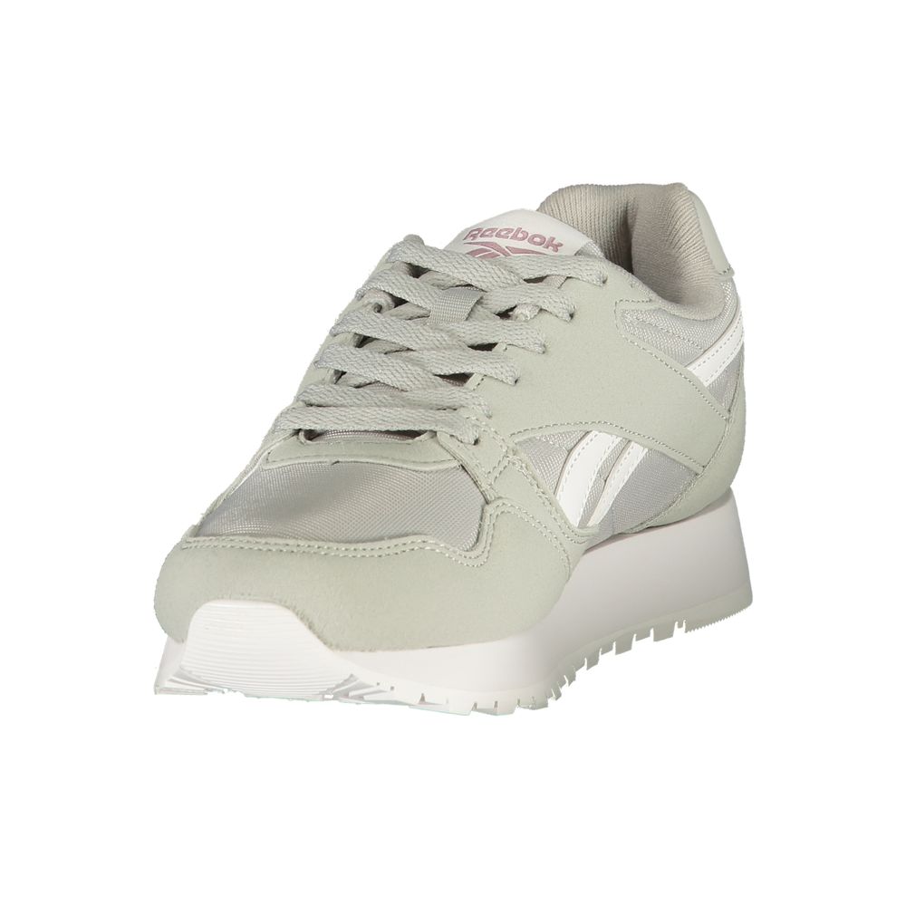 Female model wearing Reebok sage gray women's sneakers with a soft sage mixed mesh and suede upper, iconic white Reebok vector logo, subtle pink accent branding, and chunky white platform sole, captured mid-step in a casual lifestyle pose showcasing the sneaker's retro athletic silhouette and everyday versatility.