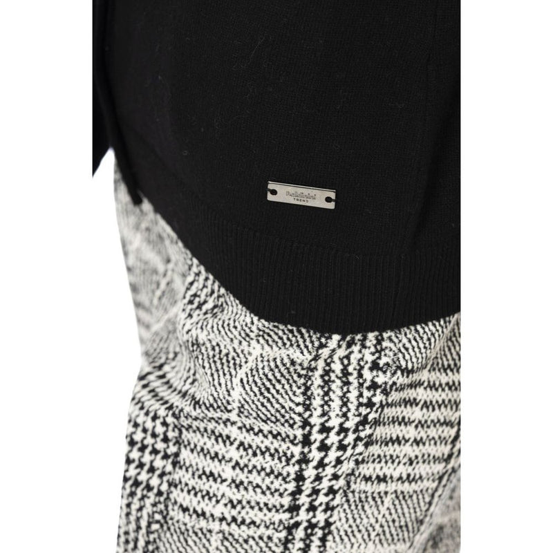 Close-up of a black knit wool cardigan with a small silver metal logo tag on the hem