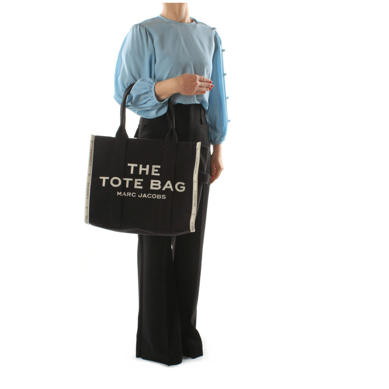 Marc Jacobs black canvas tote bag with white lettering held by a person