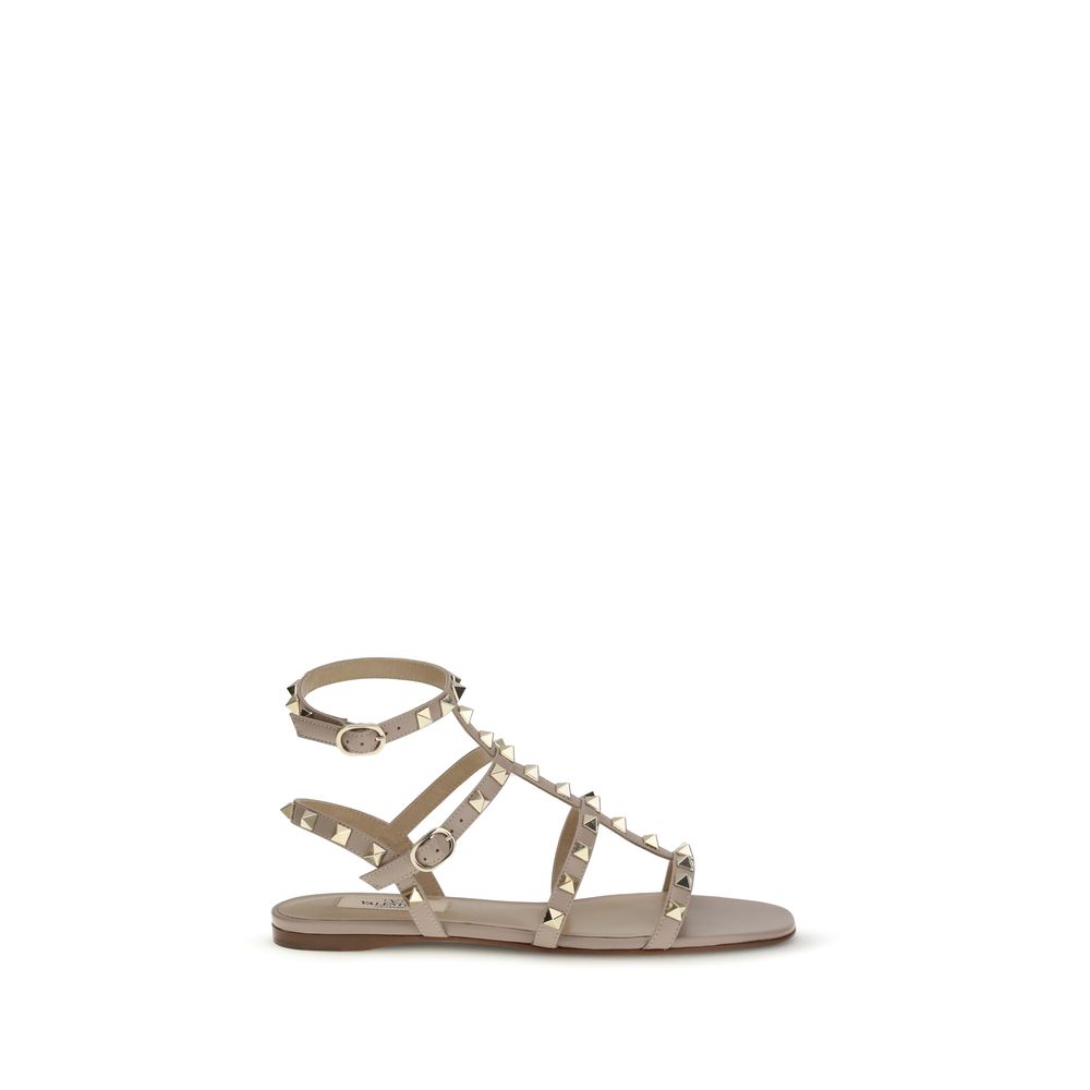 Female model wearing Valentino Garavani beige calf leather flat sandals with luxurious beige calf leather straps, delicate flat silhouette, and signature Valentino Garavani detailing, captured mid-step in a casual lifestyle pose showcasing the sandal's refined elegance and iconic Italian luxury craftsmanship.