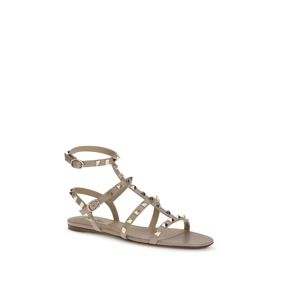 Female model wearing Valentino Garavani beige calf leather flat sandals with luxurious beige calf leather straps, delicate flat silhouette, and signature Valentino Garavani detailing, captured mid-step in a casual lifestyle pose showcasing the sandal's refined elegance and iconic Italian luxury craftsmanship.