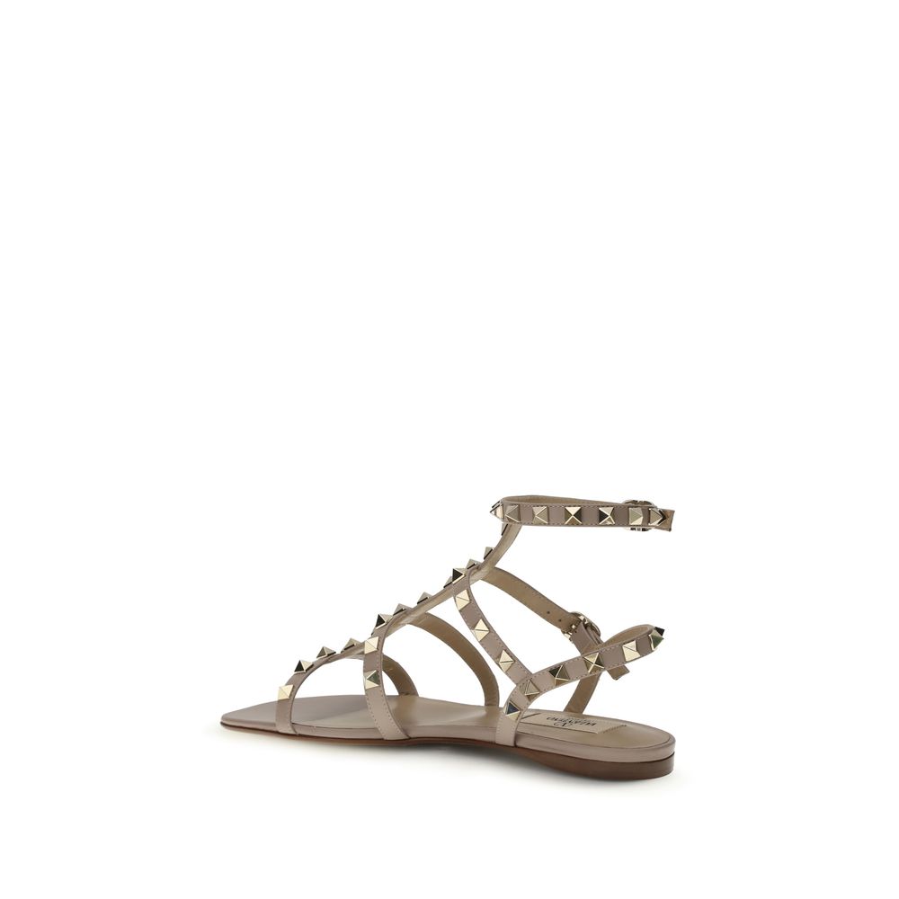 Female model wearing Valentino Garavani beige calf leather flat sandals with luxurious beige calf leather straps, delicate flat silhouette, and signature Valentino Garavani detailing, captured mid-step in a casual lifestyle pose showcasing the sandal's refined elegance and iconic Italian luxury craftsmanship.