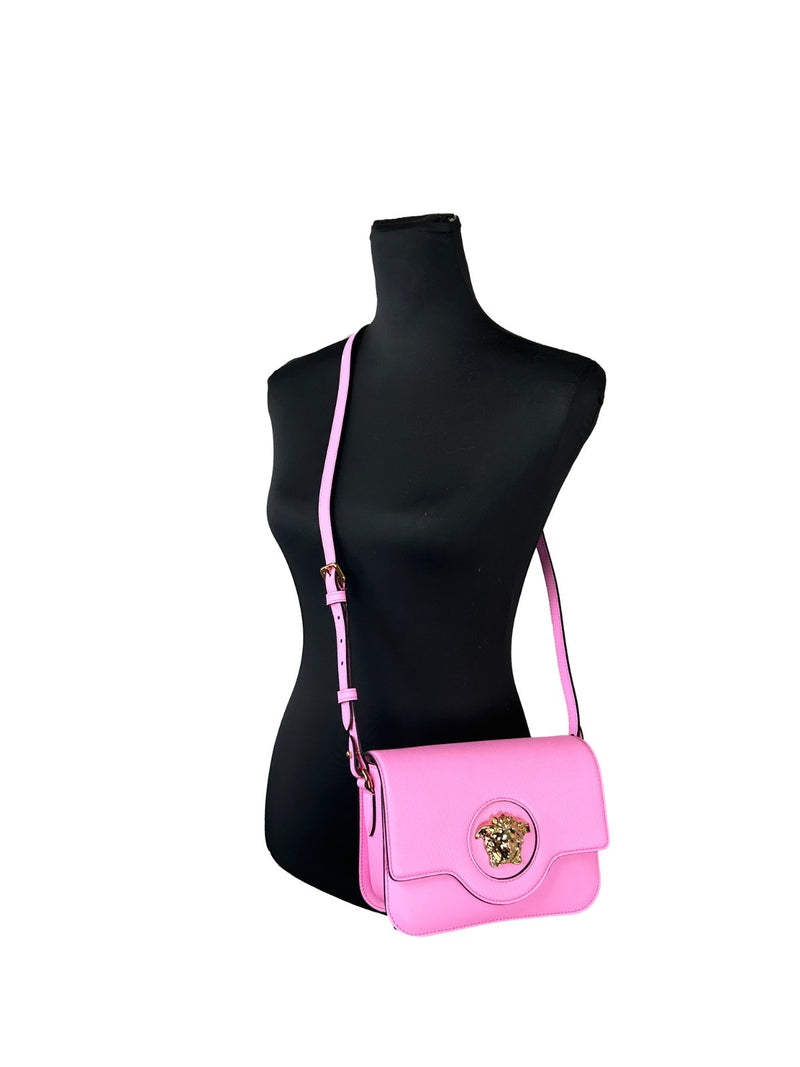 Pink leather shoulder crossbody bag with gold Medusa logo on a black mannequin