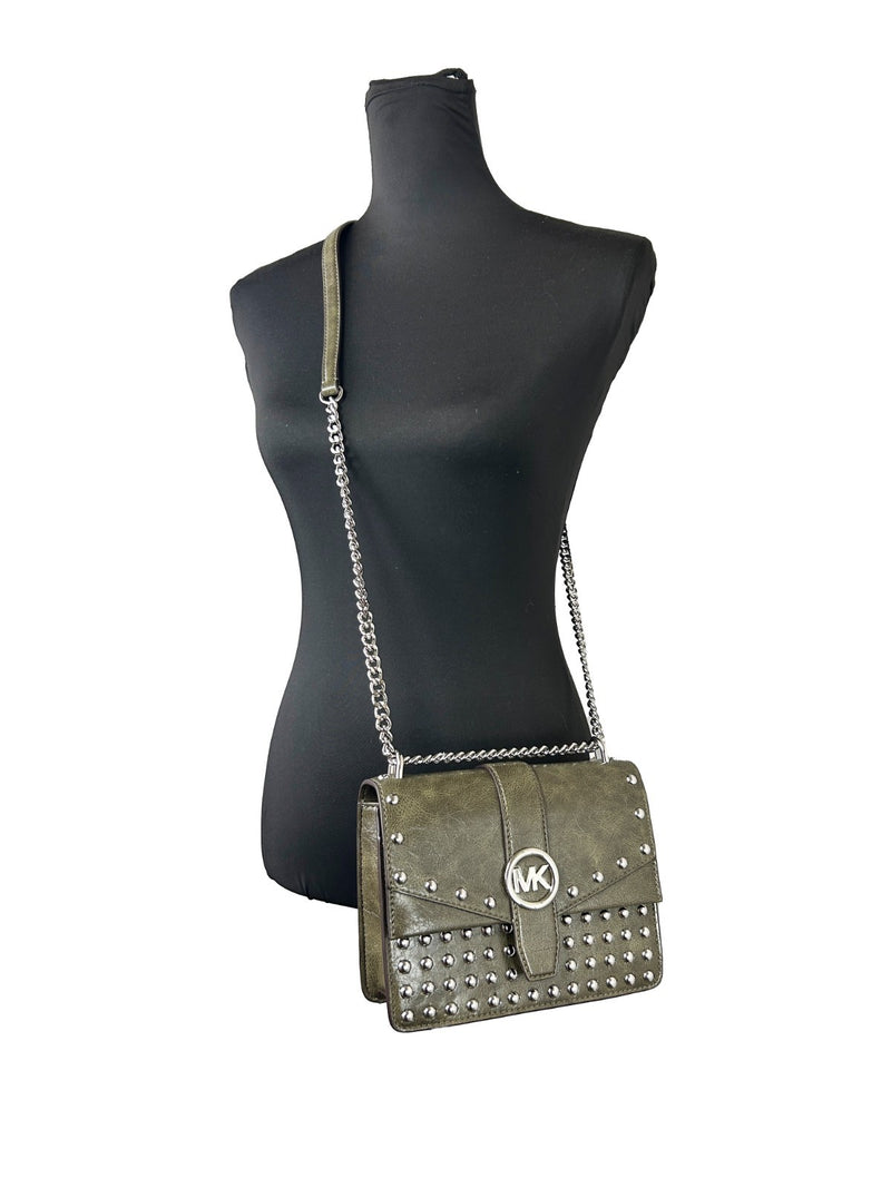 Olive green leather flap shoulder crossbody bag with silver studs and chain strap worn on black mannequin