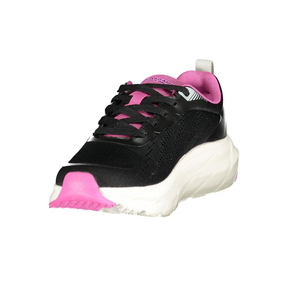 Female model wearing U.S. POLO ASSN. nero black fabric women's sneakers with a sleek dark textile upper, signature polo branding, and sporty black sole, captured mid-step in a casual lifestyle pose showcasing the shoe's bold profile and everyday athletic style.