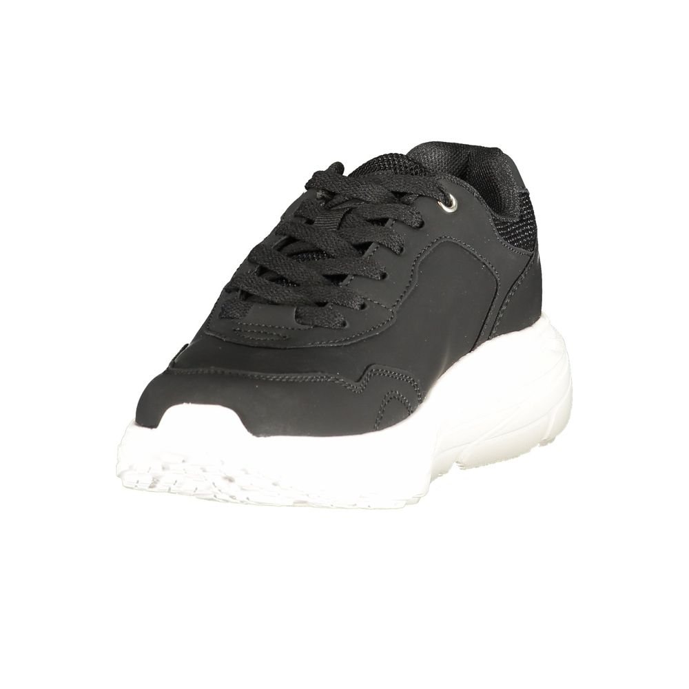 Female model wearing U.S. POLO ASSN. black polyurethane women's sneakers with a sleek black upper, signature polo branding, and sporty black sole, captured mid-step in a casual lifestyle pose showcasing the shoe's bold profile and everyday athletic style.