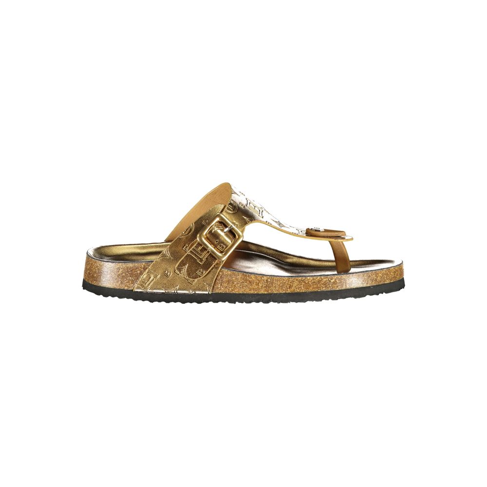 Female model wearing Norway 1963 gold metallic embossed leather thong sandal with a richly textured gold upper, adjustable side buckle strap, natural cork footbed, and black rubber outsole, captured mid-step in a casual lifestyle pose showcasing the sandal's opulent golden glamour and effortless summer luxury.