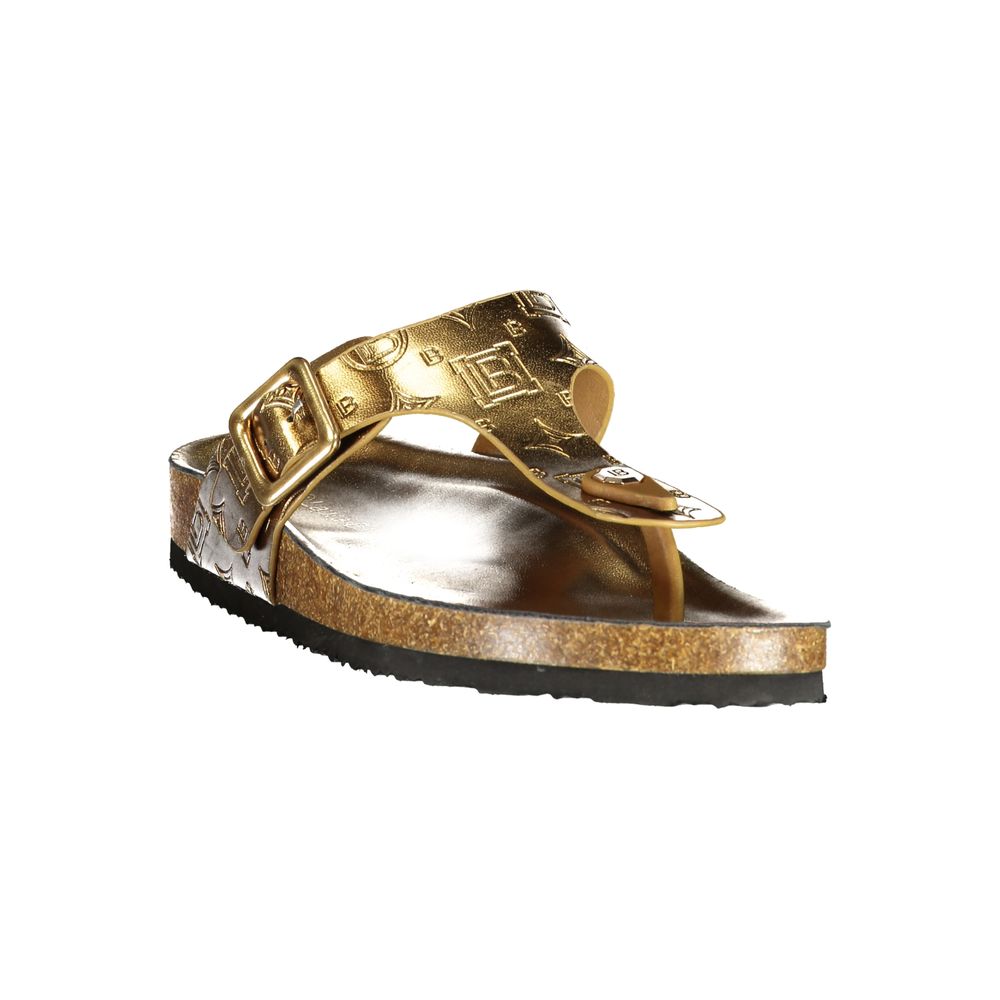 Female model wearing Norway 1963 gold metallic embossed leather thong sandal with a richly textured gold upper, adjustable side buckle strap, natural cork footbed, and black rubber outsole, captured mid-step in a casual lifestyle pose showcasing the sandal's opulent golden glamour and effortless summer luxury.