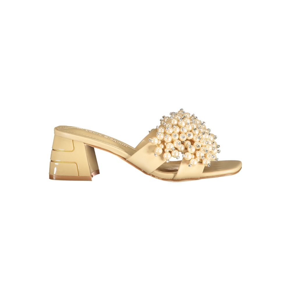 Female model wearing champagne satin mule sandal with a lavishly pearl and crystal-encrusted wide strap, square open toe, and sculptural gold block heel with geometric cut-out detailing, captured mid-step in a casual lifestyle pose showcasing the sandal's opulent bridal-luxe elegance and effortless designer glamour.
