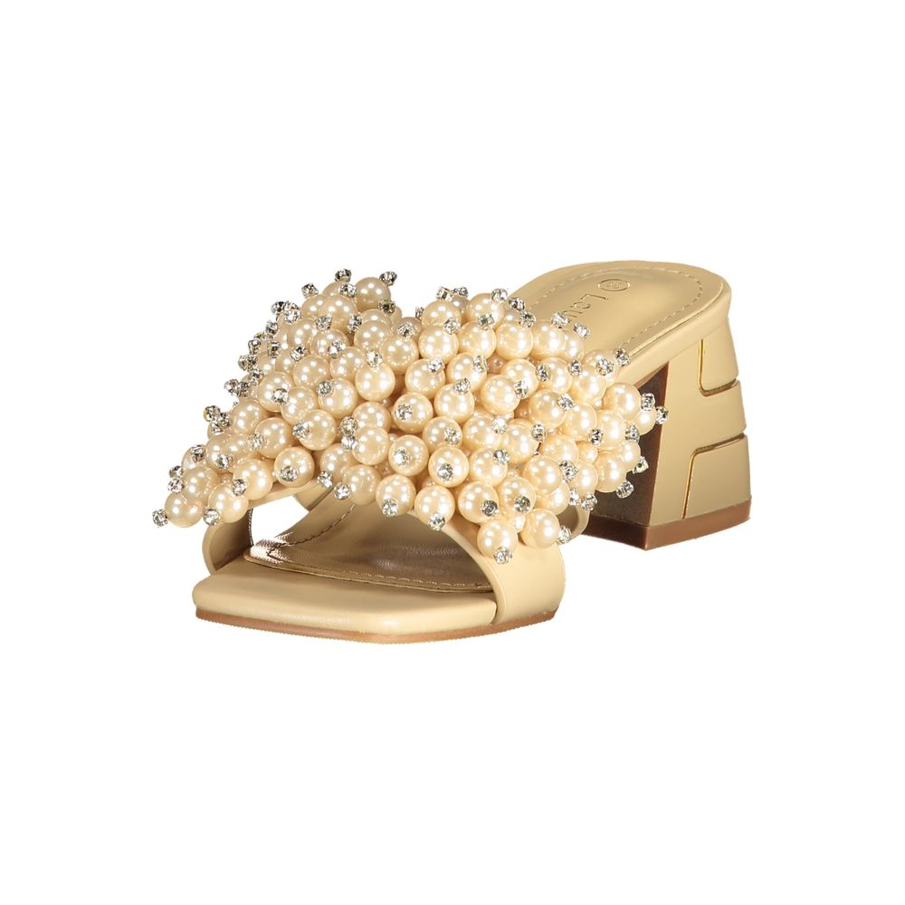 Female model wearing champagne satin mule sandal with a lavishly pearl and crystal-encrusted wide strap, square open toe, and sculptural gold block heel with geometric cut-out detailing, captured mid-step in a casual lifestyle pose showcasing the sandal's opulent bridal-luxe elegance and effortless designer glamour.