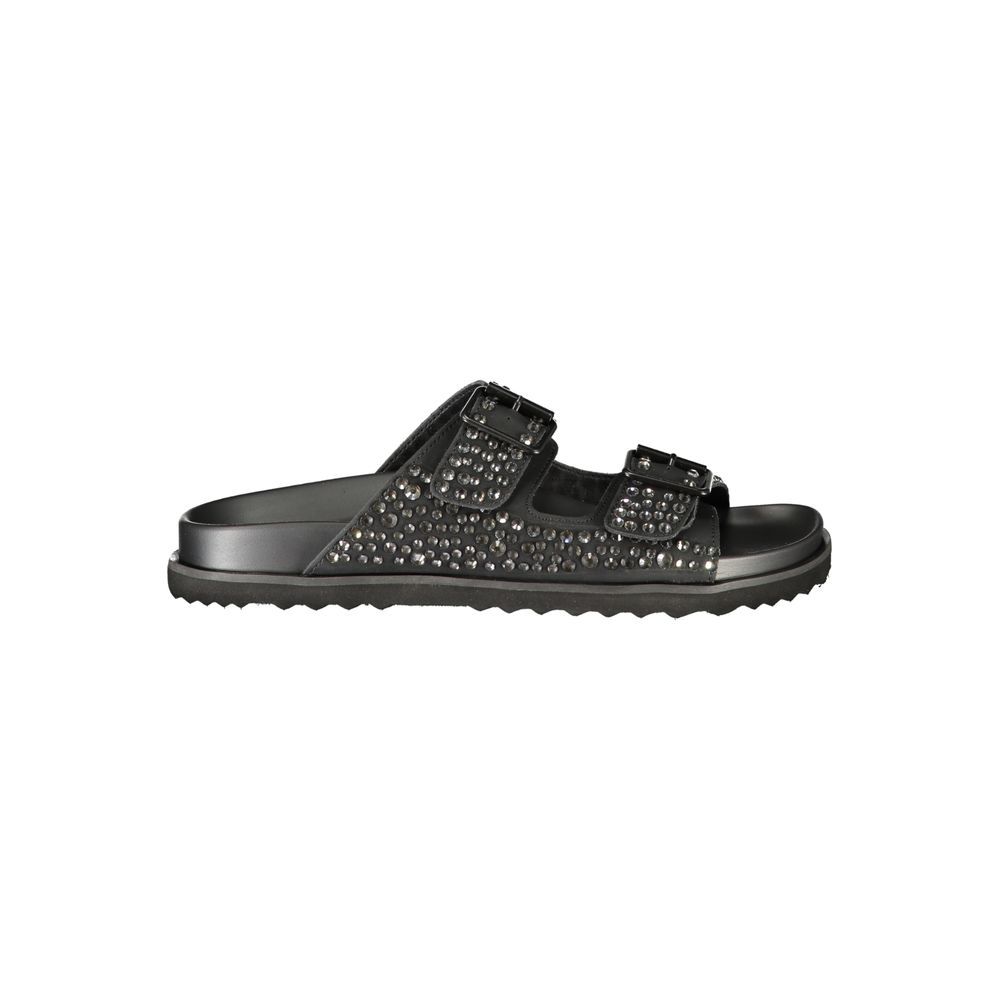 Female model wearing black double-strap slide sandal with two wide straps densely encrusted with gunmetal crystal rhinestones, dual adjustable buckle closures, and a sleek black ridged outsole, captured mid-step in a casual lifestyle pose showcasing the sandal's bold crystal-embellished glamour and effortless rock-luxe edge