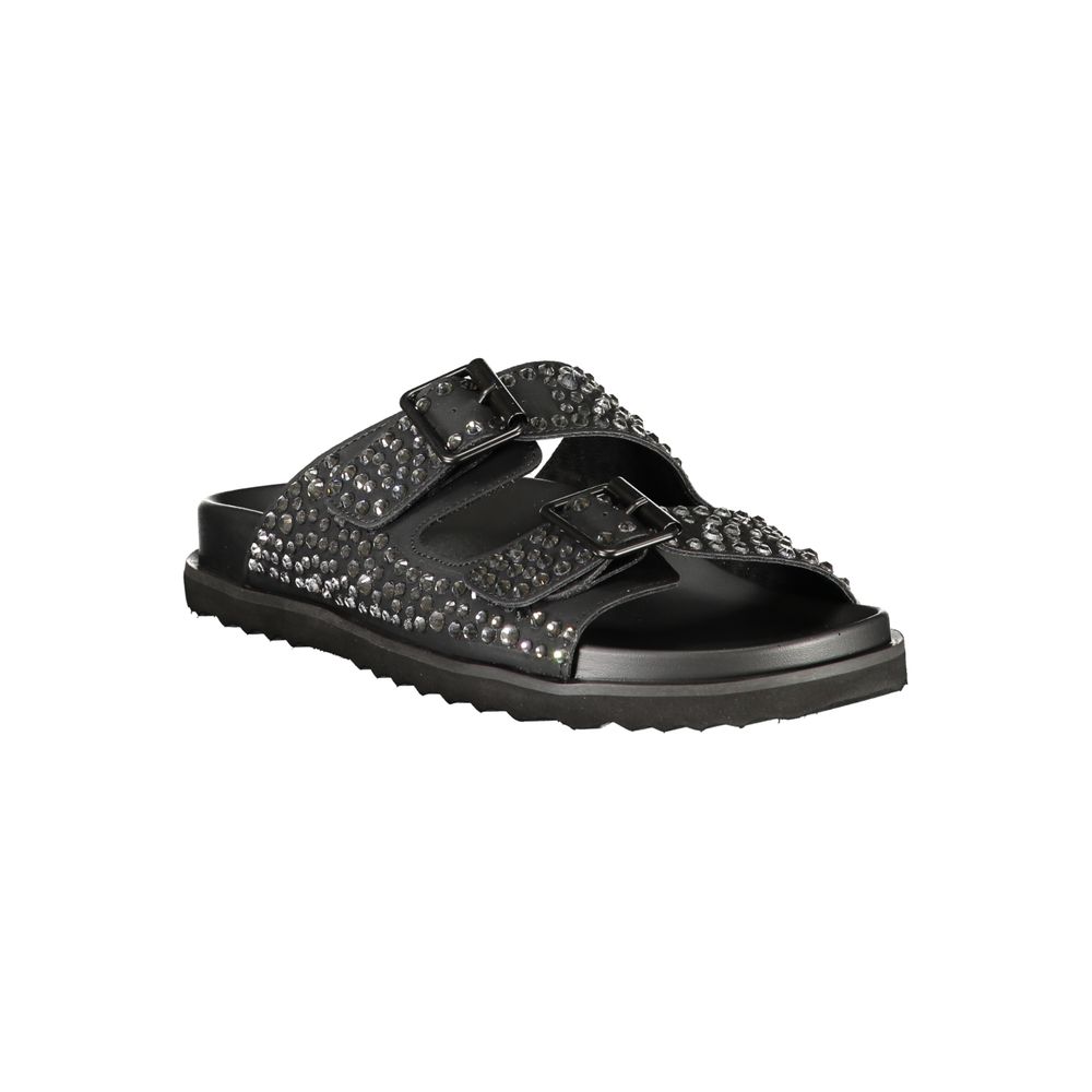 Female model wearing black double-strap slide sandal with two wide straps densely encrusted with gunmetal crystal rhinestones, dual adjustable buckle closures, and a sleek black ridged outsole, captured mid-step in a casual lifestyle pose showcasing the sandal's bold crystal-embellished glamour and effortless rock-luxe edge