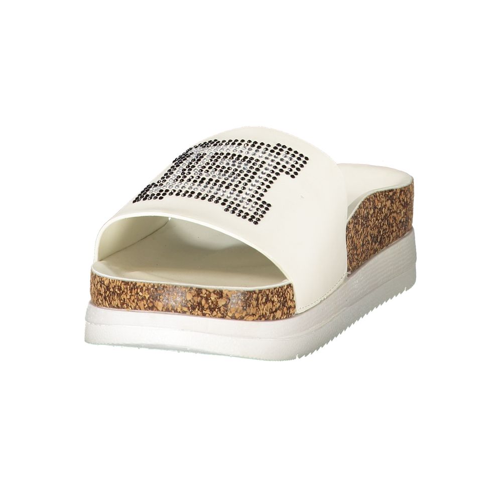 Female model wearing Laura Biagiotti white polyethylene slippers with a wide white upper band adorned with rhinestone crystal embellishment, cork-effect platform midsole, and white rubber outsole, captured mid-step in a casual lifestyle pose showcasing the slipper's glamorous summer style and Italian designer flair.