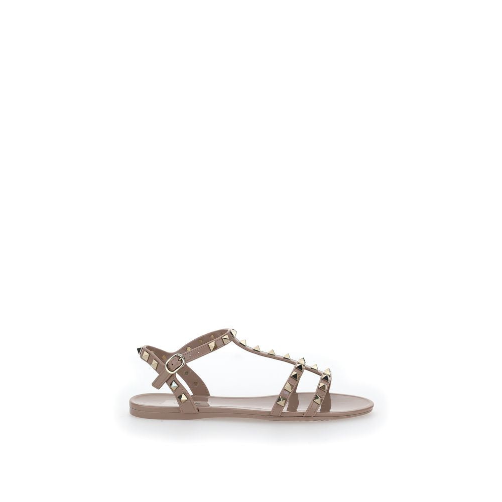 Female model wearing Valentino Garavani pink PVC flat sandals with vibrant pink PVC straps, delicate flat silhouette, and signature Valentino Garavani detailing, captured mid-step in a casual lifestyle pose showcasing the sandal's bold feminine charm and iconic Italian luxury craftsmanship.
