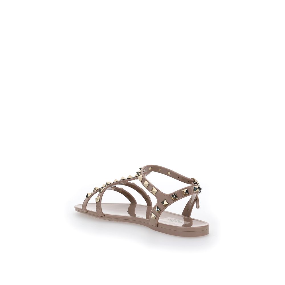 Female model wearing Valentino Garavani pink PVC flat sandals with vibrant pink PVC straps, delicate flat silhouette, and signature Valentino Garavani detailing, captured mid-step in a casual lifestyle pose showcasing the sandal's bold feminine charm and iconic Italian luxury craftsmanship.