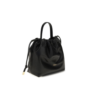 Chloé black leather shoulder bag with a top handle, drawstring closure, and gold-tone logo.