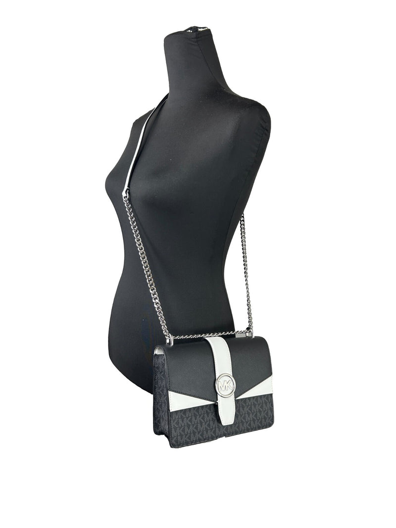 Black and white monogram canvas flap crossbody bag with silver chain strap worn on a mannequin