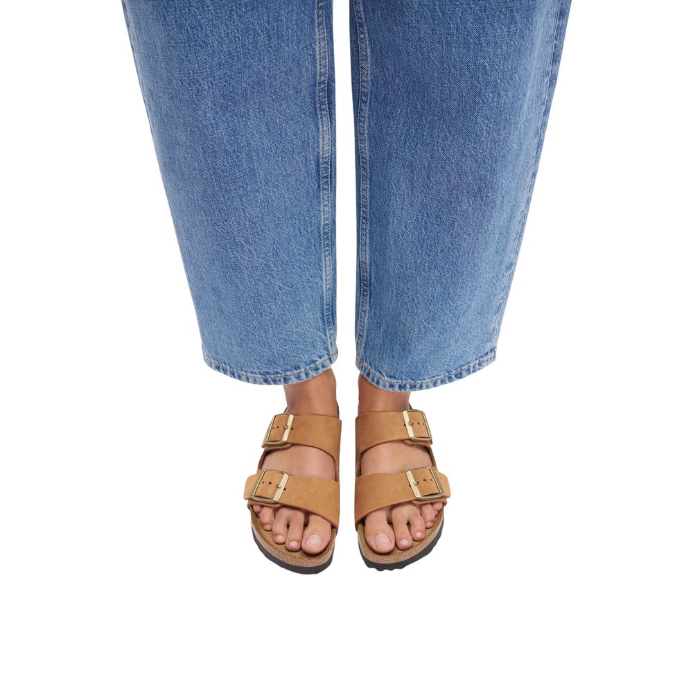 Tan suede double-strap sandals with gold buckles worn with blue jeans.