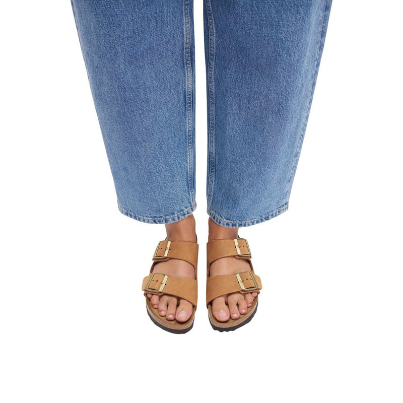 Tan suede double-strap sandals with gold buckles worn with blue jeans.