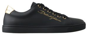 Black leather Dolce & Gabbana low-top sneaker with gold logo script, gold eyelets, and a metallic gold heel tab.