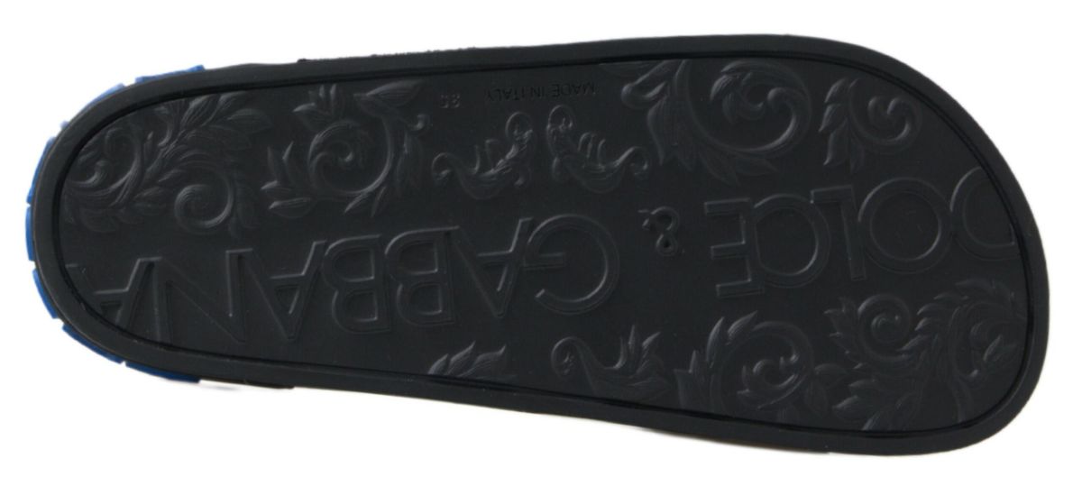 Black rubber Dolce & Gabbana slide sandal sole with embossed logo and floral pattern, featuring a blue heel accent.