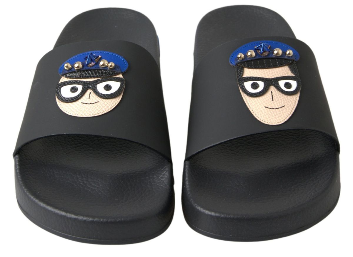 Black rubber slide sandals with a cartoon character appliqué wearing a blue cap and glasses on the wide strap.