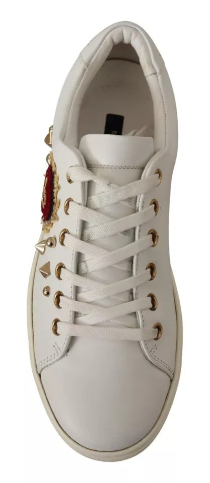 White leather Dolce & Gabbana sneakers with gold eyelets, pyramid studs, and a red heart appliqué.