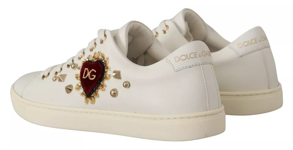 White leather Dolce & Gabbana sneakers with a red heart appliqué, gold studs, and gold logo detailing.