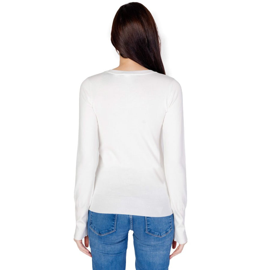 White cotton long-sleeve V-neck sweater with buttoned cuffs worn with blue jeans