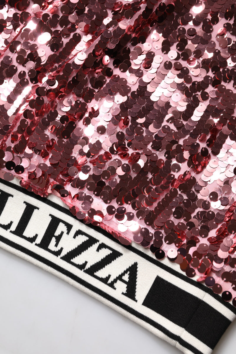 Close-up of a pink sequin pullover sweater with a wide black and white ribbed hem featuring text