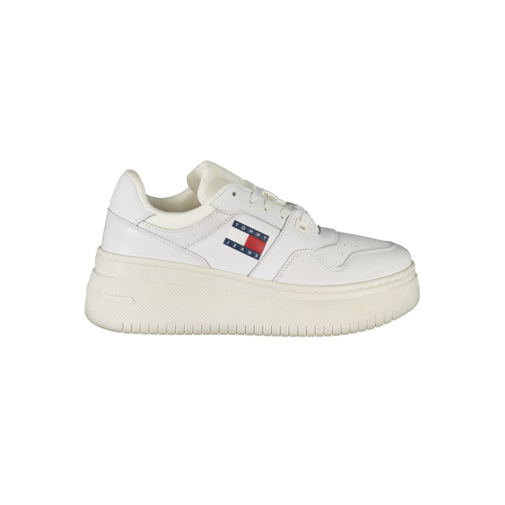 Female model wearing Tommy Hilfiger bianco white leather women's sneakers with a clean white leather upper, classic Tommy Hilfiger flag branding, and sporty white sole, captured mid-step in a casual lifestyle pose showcasing the sneaker's timeless preppy style and everyday versatility.