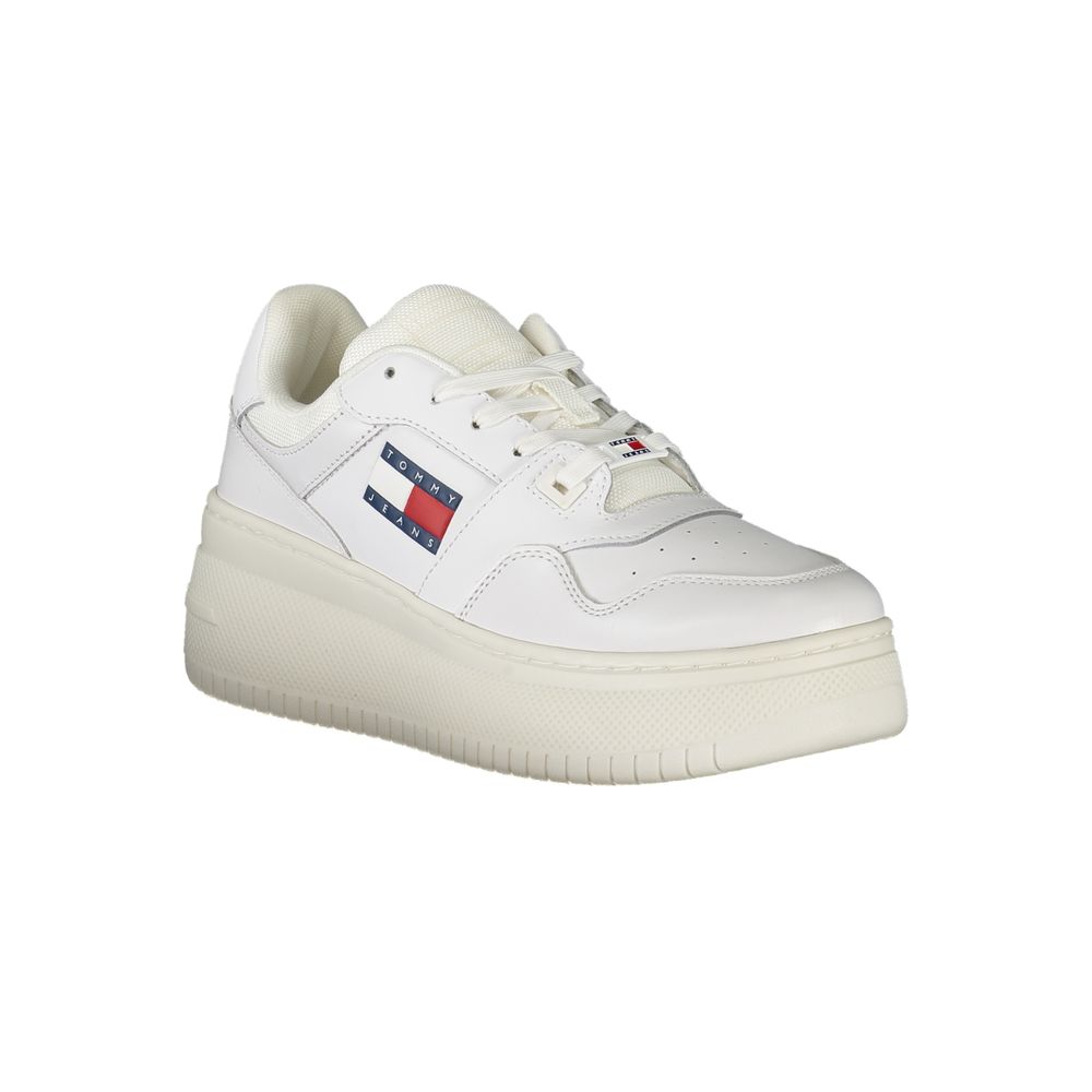 Female model wearing Tommy Hilfiger bianco white leather women's sneakers with a clean white leather upper, classic Tommy Hilfiger flag branding, and sporty white sole, captured mid-step in a casual lifestyle pose showcasing the sneaker's timeless preppy style and everyday versatility.