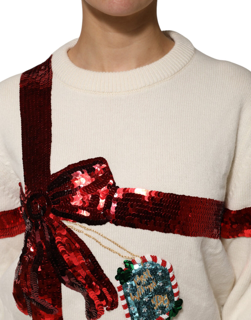 White knit crew neck sweater with a large red sequined gift bow and tag