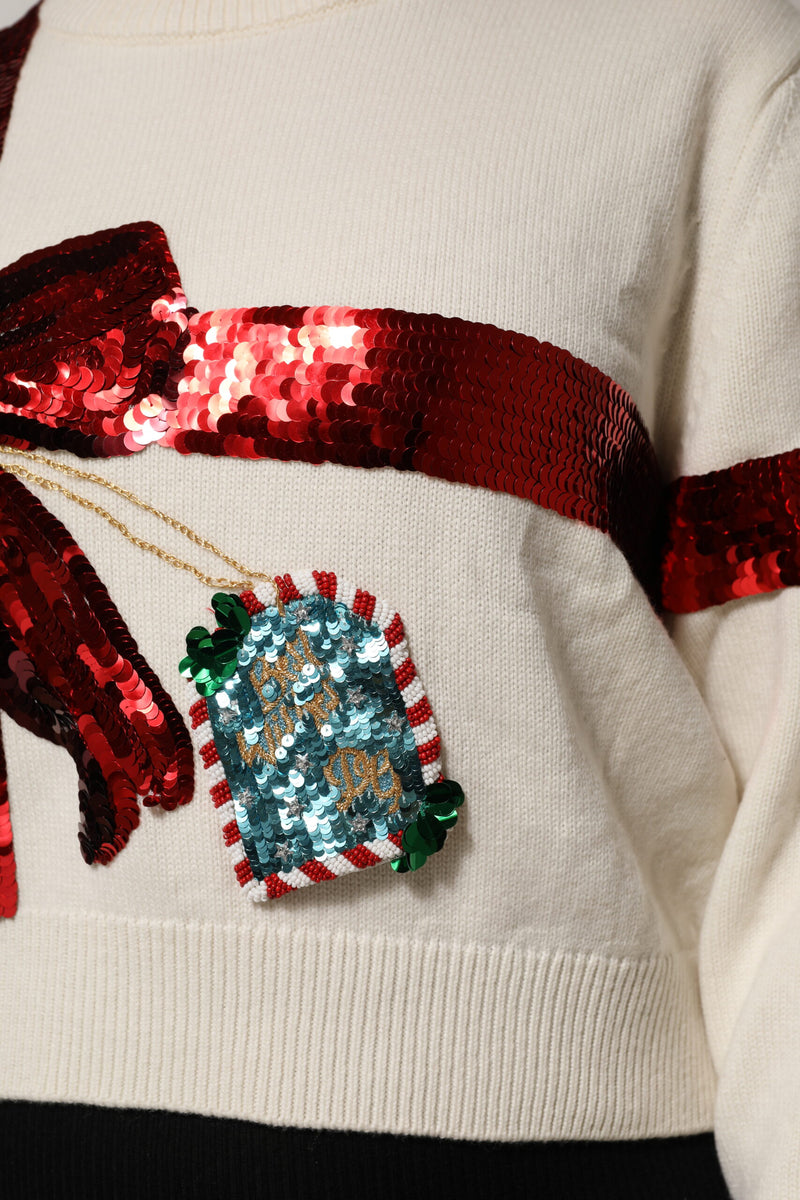 White knit crew-neck sweater with a large red sequined gift bow and tag