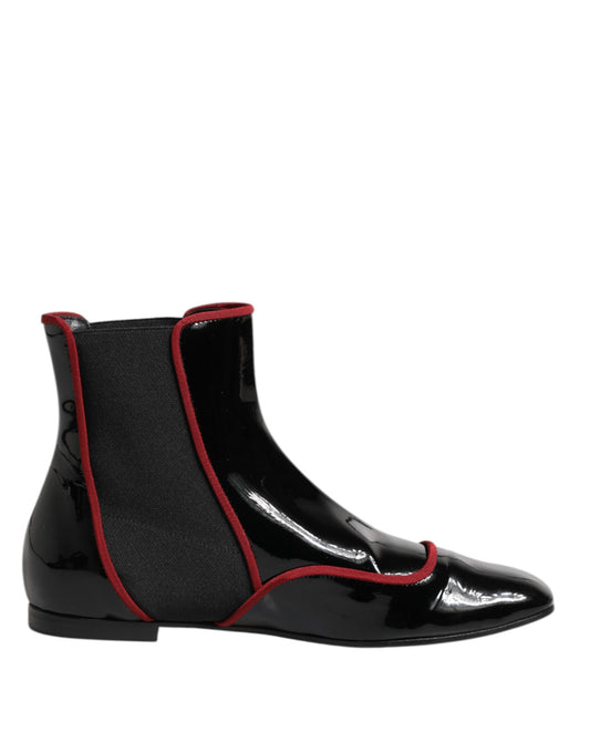 Black patent leather Chelsea boots with red trim piping and elastic side panels on a flat sole.