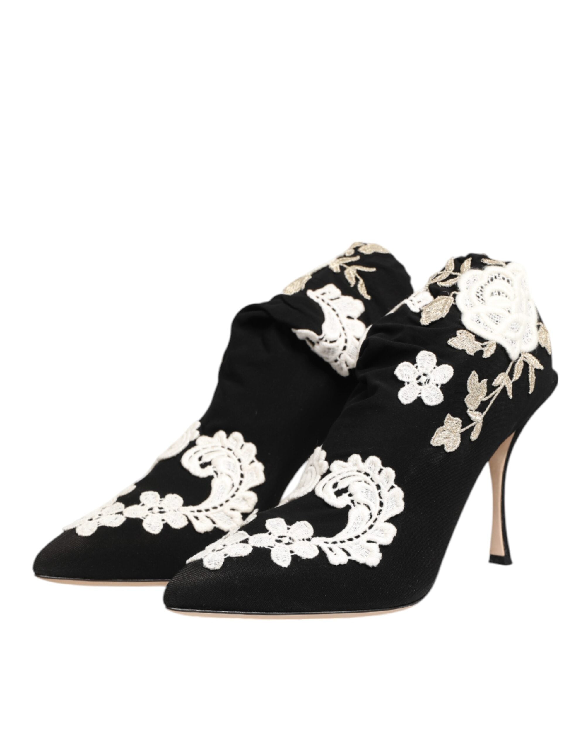 Black satin pointed-toe ankle boots with ruched detailing and ornate white floral lace embroidery and stiletto heels.