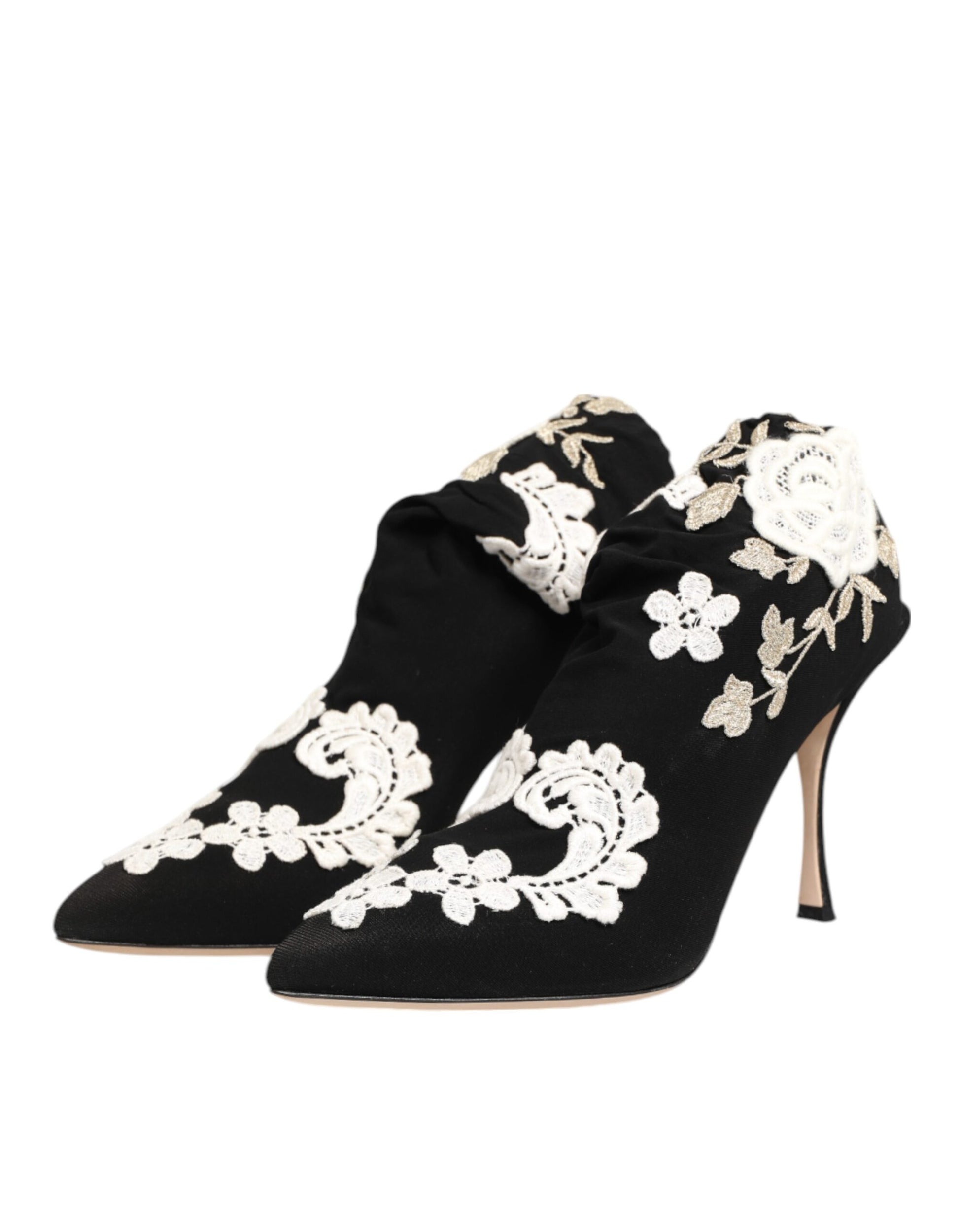 Black satin pointed-toe ankle boots with ruched detailing and ornate white floral lace embroidery and stiletto heels.